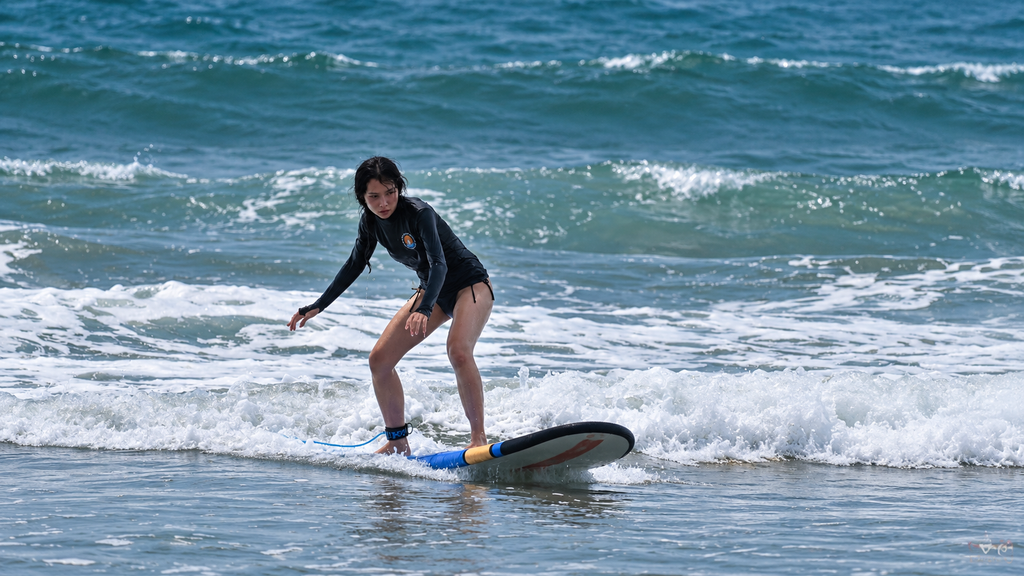 Beginner surfer standing on a board in small waves near Canggu beach, Bali.
